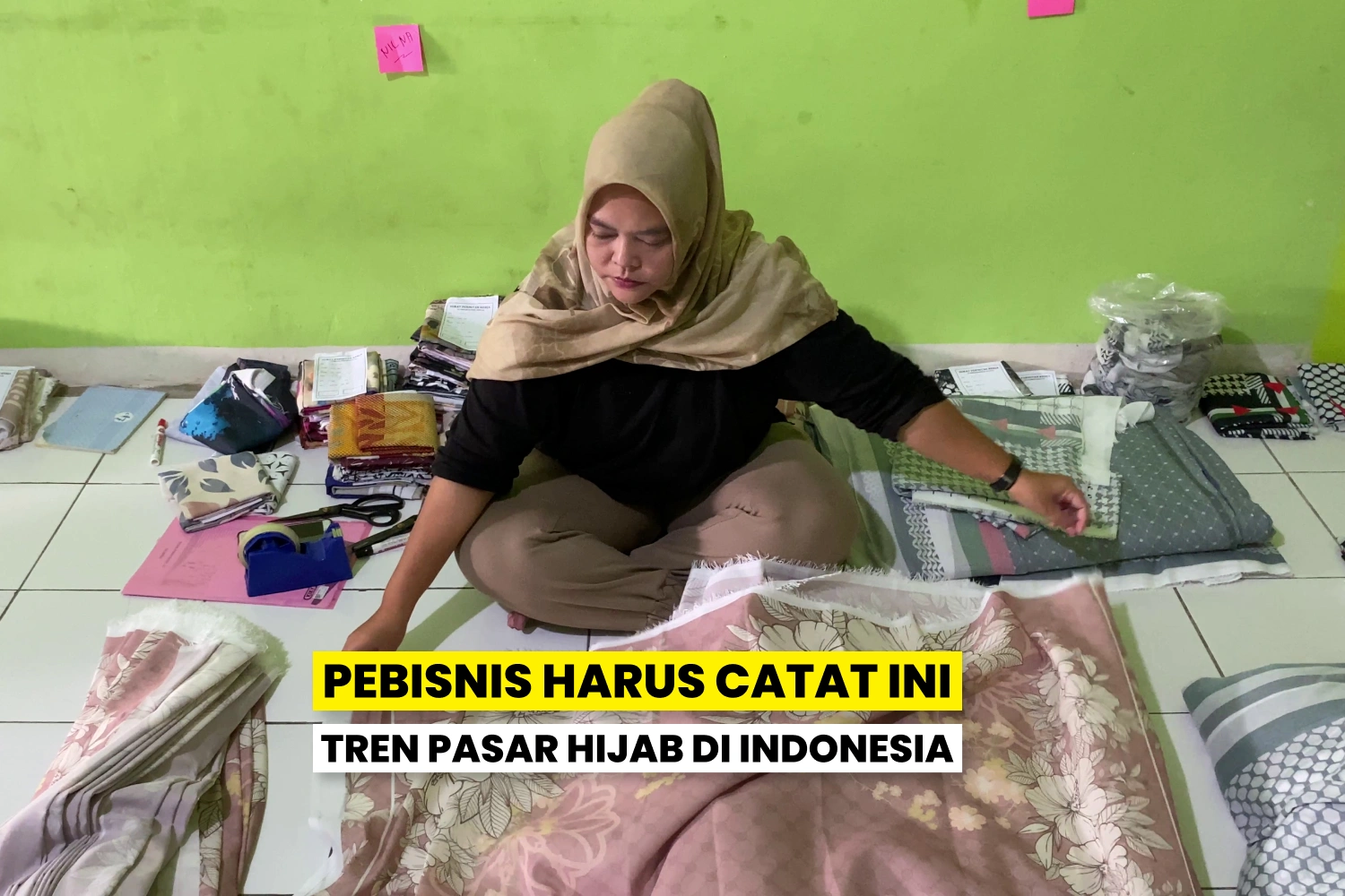 Seorang perempuan berhijab sedang memilih kain di antara tumpukan kain, mencerminkan tren pasar hijab di Indonesia.